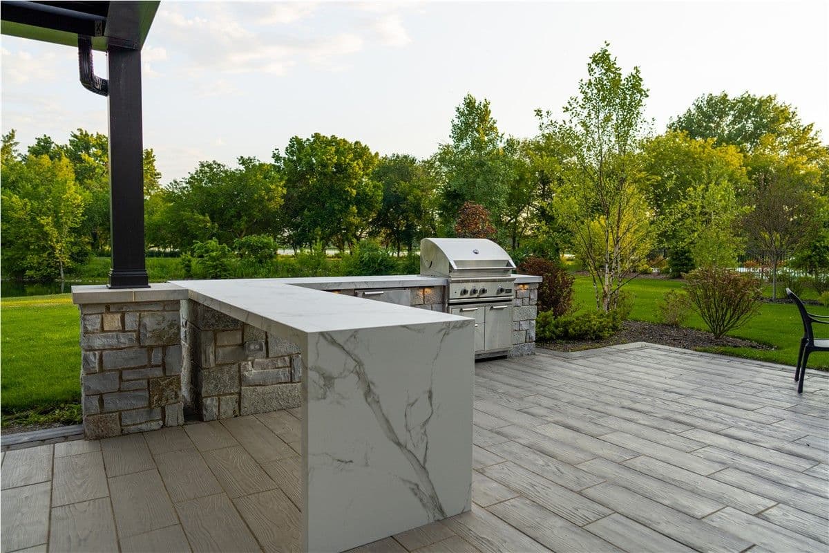 A stone outdoor grilling station and white and gray marbled counterspace on a patio.